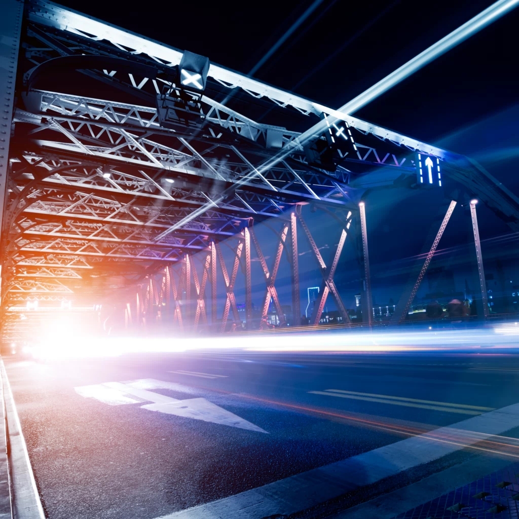 Nachtszene einer beleuchteten Stahlbrücke mit Lichtspuren – Symbol für Geschwindigkeit und moderne Infrastruktur